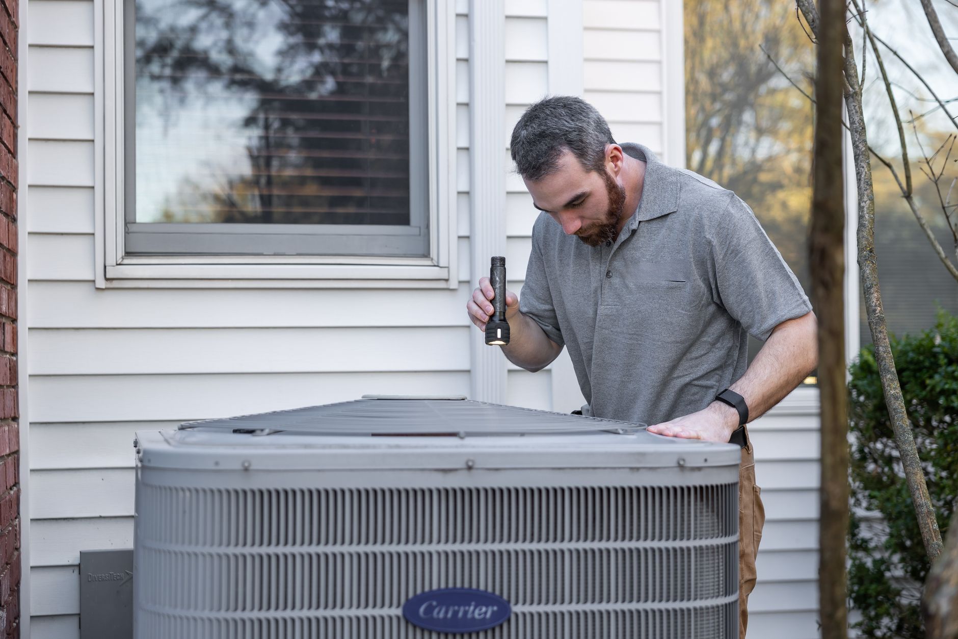 A technician inspects an outdoor HVAC condenser unit.