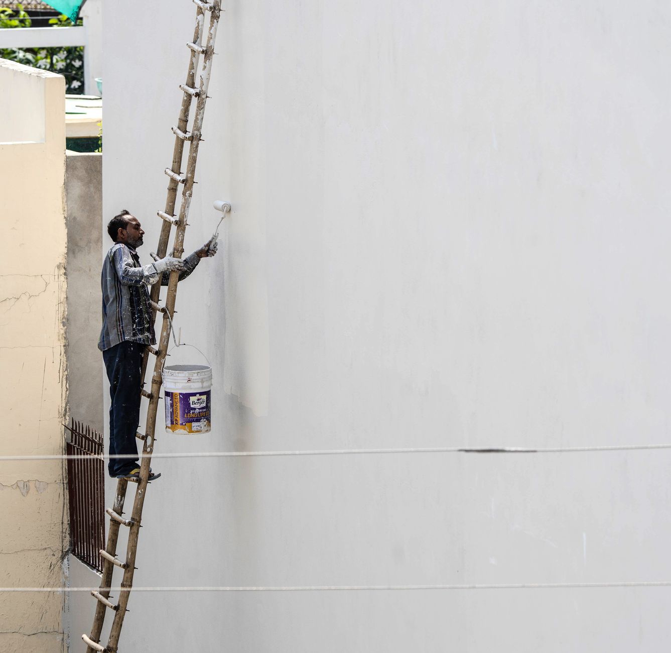 A painter on a ladder applying paint to an exterior wall with a roller
