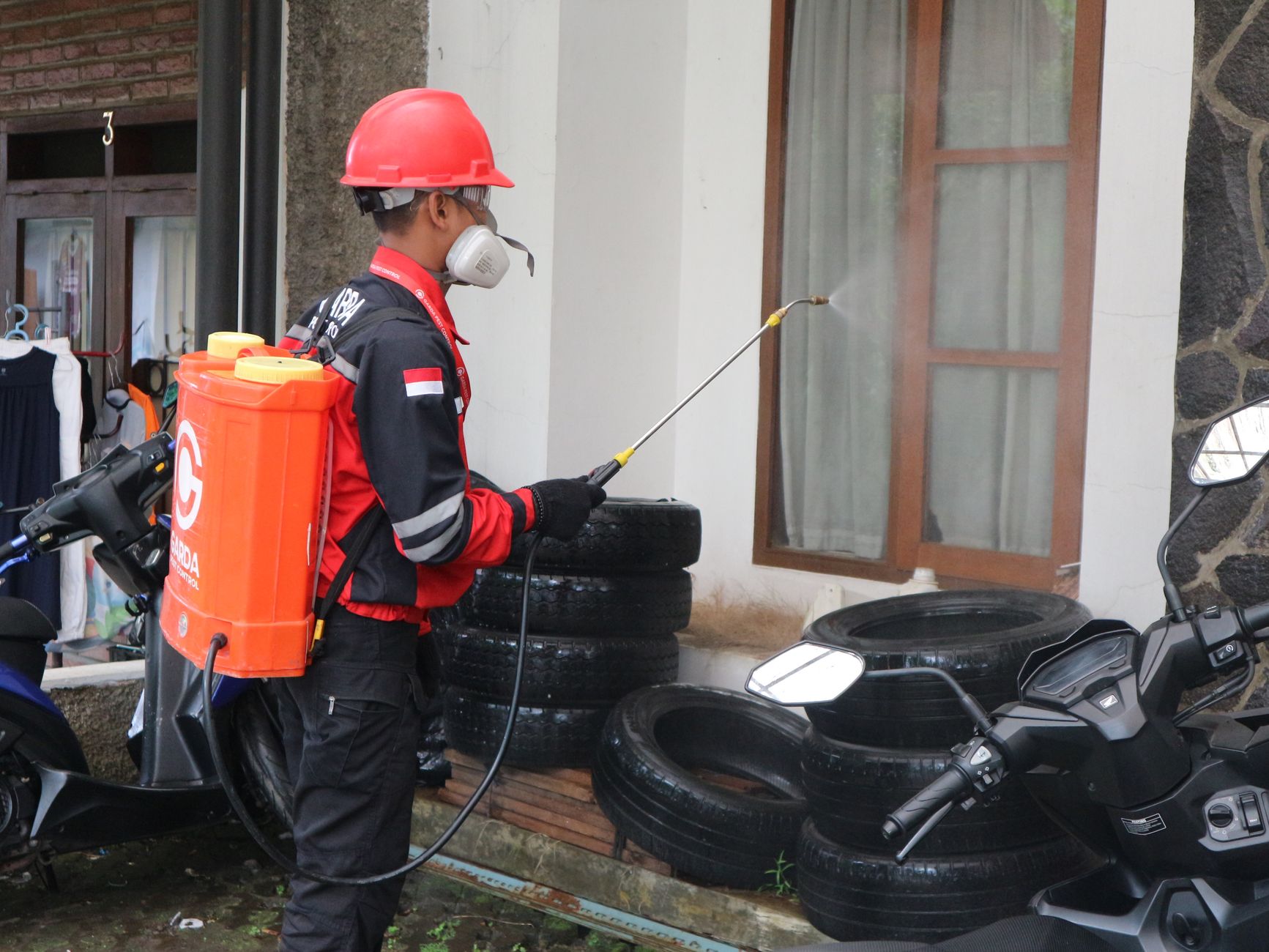 A pest control technician in protective gear spraying the exterior of a building