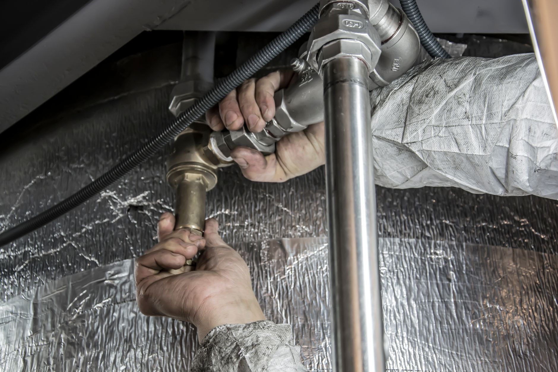 Close-up of a plumber's hands installing steel pipes indoors.
