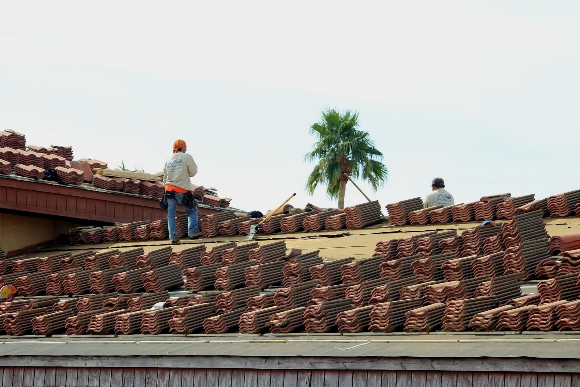 Workers installing terra cotta roof tiles under a sunny sky.