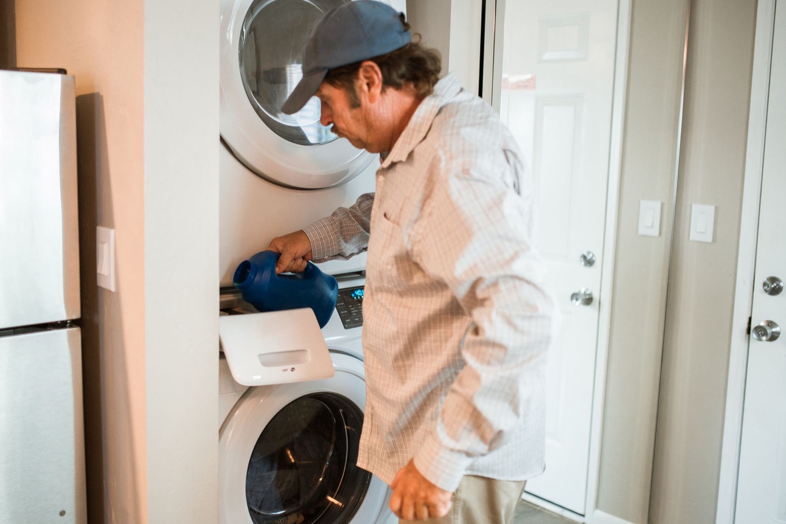 A uniformed appliance technician servicing a stacked washer and dryer in a home laundry closet