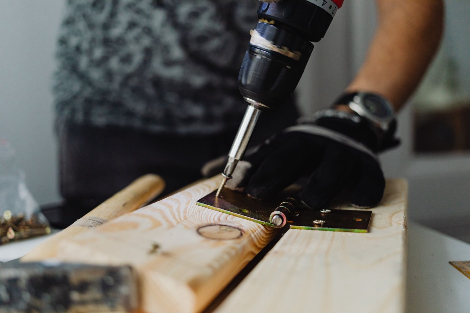 A handyman driving a screw into a wood board with a cordless drill